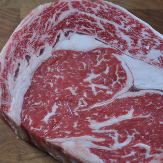 A close-up of a raw marbled steak on a wooden cutting board.